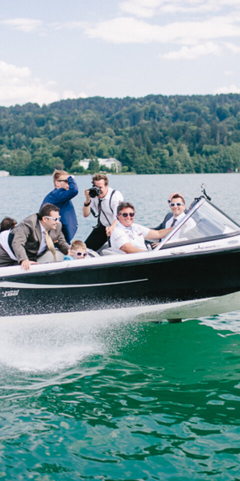 <p>Gruppe von jungen Männern als Partygesellschaft auf einem gleitenden Motorboot im türkisen Wörthersee.</p>